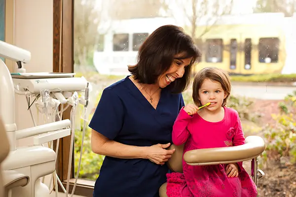 A dental hygienist with a child patient demonstrating how to brush their teeth.