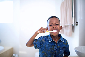 A young Black child demonstrating how to brush their teeth at home.