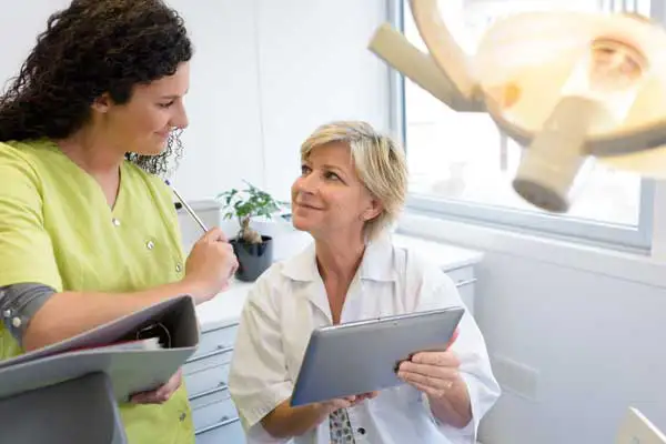 An old woman holding a tab with insurance information while a hygienist explains it to her at East Portland Dentistry 