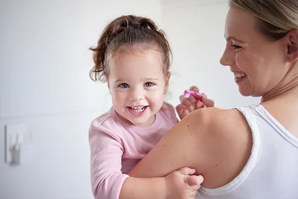 Mother teaching happy girl dental hygiene  baby toothbrush and mom holding kid  baby toothbrush and mom holding kid. Clean teeth  home healthcare and portrait of child growth. Laugh in children bathroom  healthy mouth and natural smile