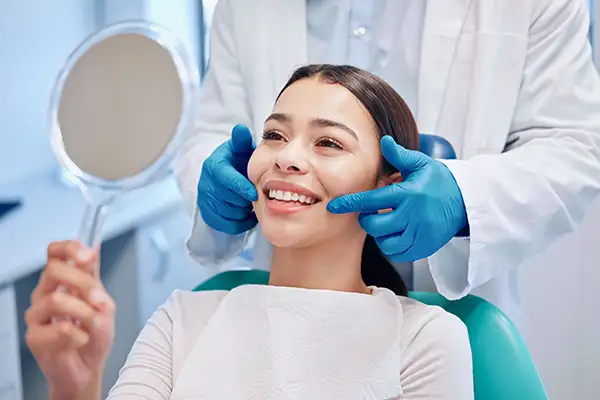 A dentist holding a smile for a patient while she looks at it in the mirror.