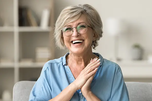 Cheerful pretty older woman in elegant glasses sitting on cozy home couch.