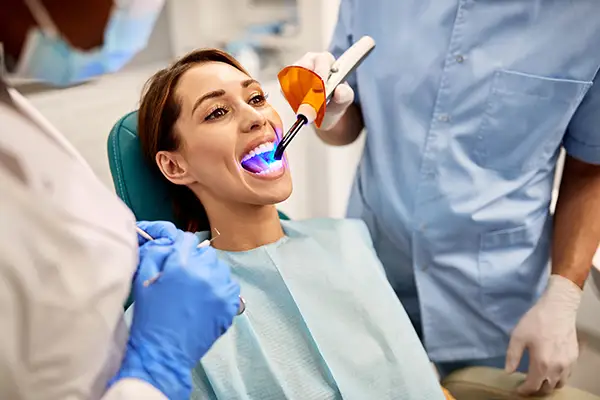 Dentist and assistant performing a dental bonding procedure on a female patient.