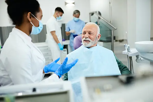 Older white patient sitting in dental chair calmly discussing his oral health with his Black female dentist East Portland Dentistry dentist visit.