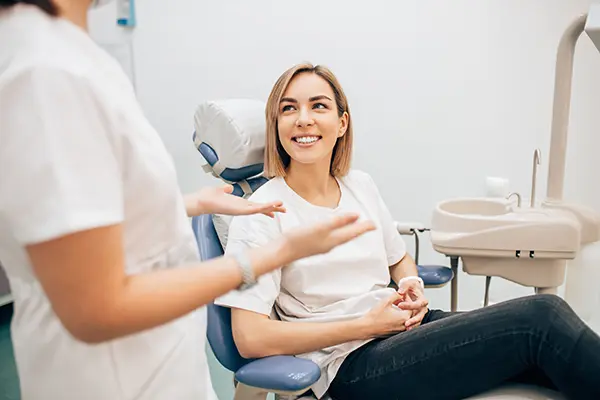 Smiling patient sitting a dental chair while her dental assistant speaks with her at East Portland Dentistry